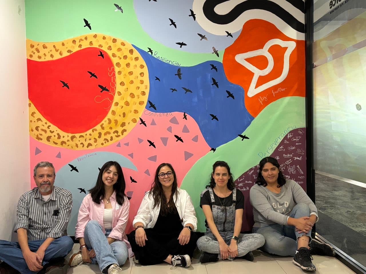 Equipo de una empresa sentado frente al mural que pintaron juntos en su taller con Mirari.